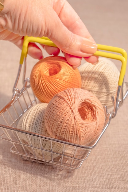 A woman\'s hand holds a metal basket with balls of knitting\
thread.