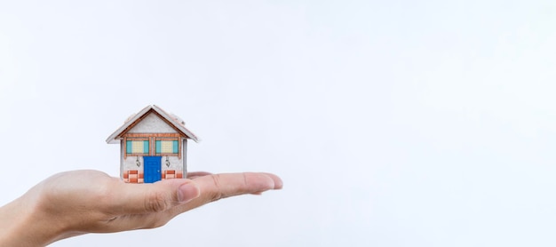 A woman's hand holds a mockup or miniature of a residential building white isolated background Purchase and sale of real estate