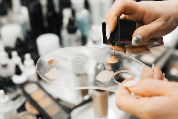 A woman's hand holds a palette and squeezes a cosmetic product, a foundation, onto it. close-up