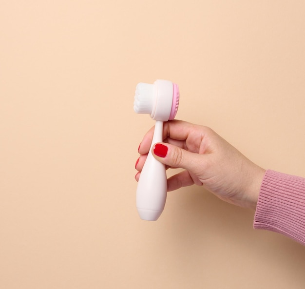 A woman's hand holds a plastic brush for face and body on a beige background