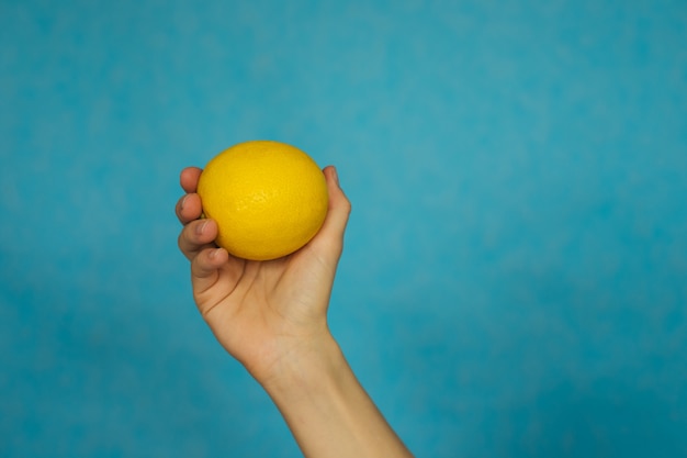 A woman's hand holds a ripe lemon on a blue background.