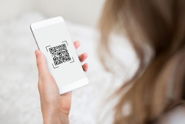 A woman's hand holds a smartphone with a qr code on the screen on a white room background