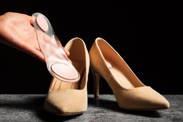 A woman's hand holds a soft orthopedic silicone insole in her hand next to a pair of classic highheeled shoes