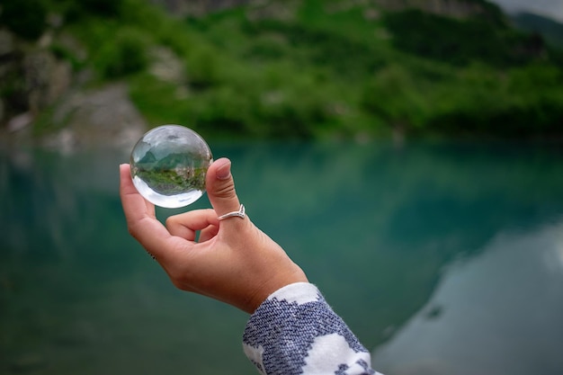 女性の手は、美しい山の湖を背景に球形のガラス玉を持っています