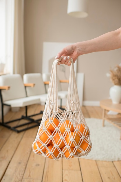 A woman's hand holds a string bag with oranges