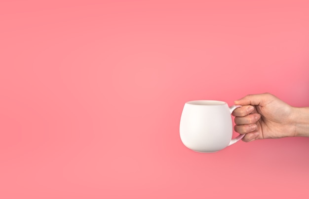 Photo a woman's hand holds a white mug on a pink background