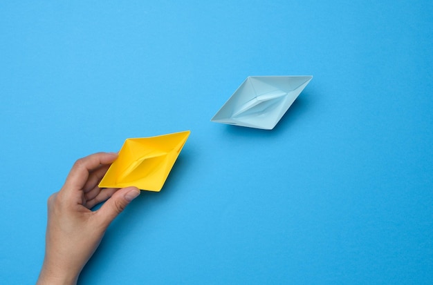 A woman's hand holds a yellow paper boat next to it is blue