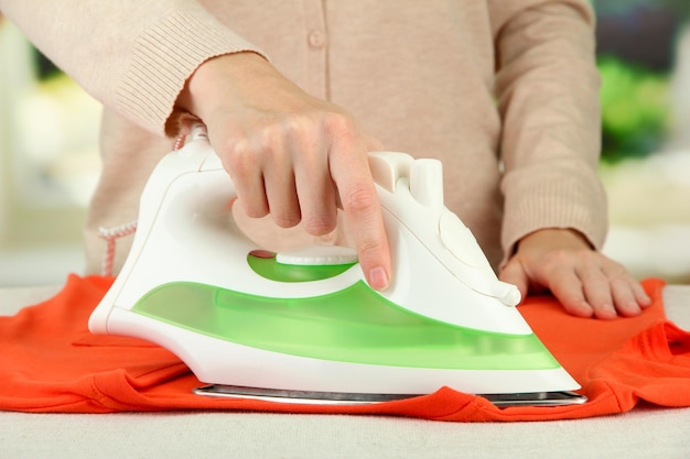 Woman's hand ironing clothes on bright background