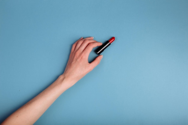 The woman's hand is taking red lipstick isolated On the blue background