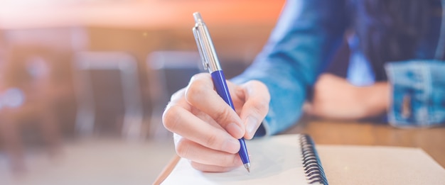 A woman's hand is writing in empty spiral notepad with a pen.Web banner