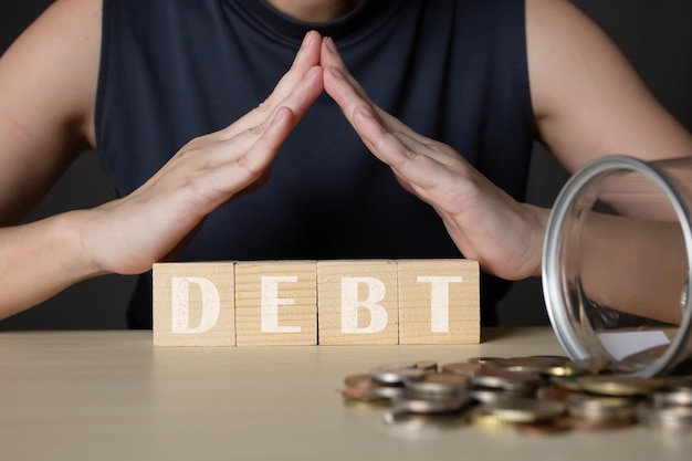 Woman's hand makes home roof gesture above wooden blocks with Debt word and coin Banking and finance concept Interest rate