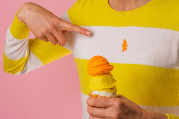 A woman's hand pointing to a dirty strawberry ice cream stain on a t-shirt