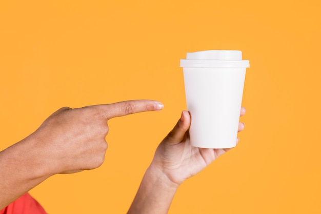 Photo woman's hand pointing over disposable cup on colored surface