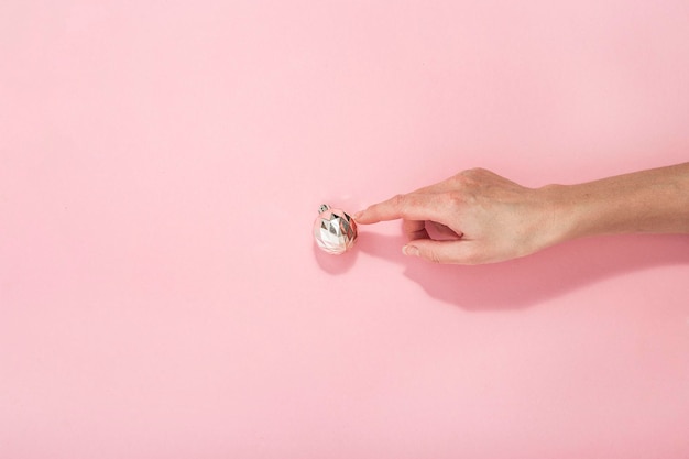 Woman's hand points to one decorative ball on a pink background Top view flat lay