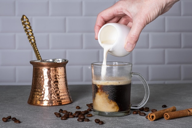 A woman's hand pours cream into a glass cup with coffee