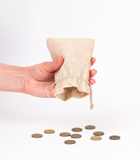 A woman's hand pours out the remains of coins from a canvas bag on a white background closeup