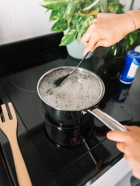 La mano della donna che prepara l'alimento in padella della salsa sulla stufa elettrica