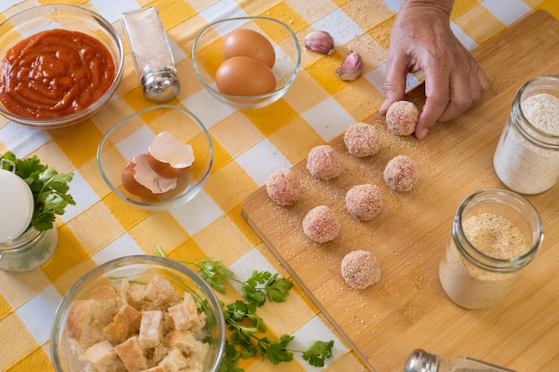 Woman's hand preparing fresh meatballs ready to be cooked, wooden cutting board and raw ingredients