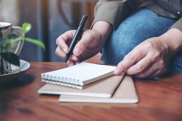 写真 木製のテーブルの上のコーヒーカップと空白のノートに書く準備をしている女性の手