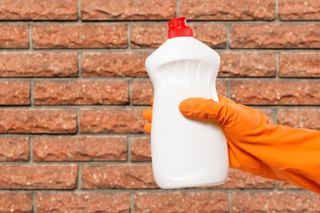 Woman's hand in protective glove with bottle of dishwashing liquid