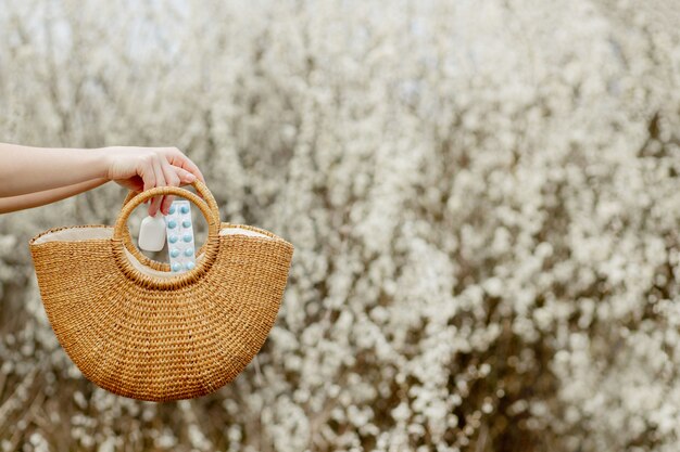 Woman's hand puts allergy pills in bag on blooming background