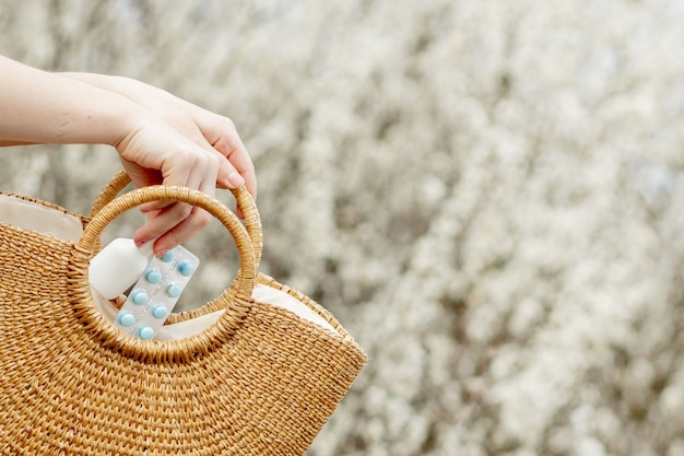 Woman's hand puts allergy pills in bag on blooming.