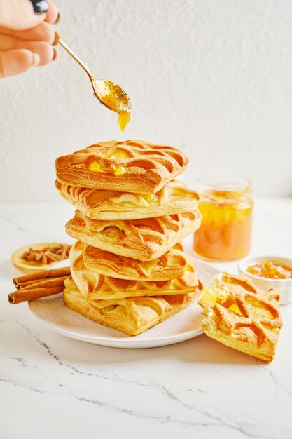 Woman's hand puts a spoon of citrus jam on stack of puff pastry