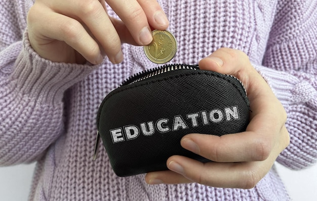 Woman's hand putting coin in black wallet with word Education