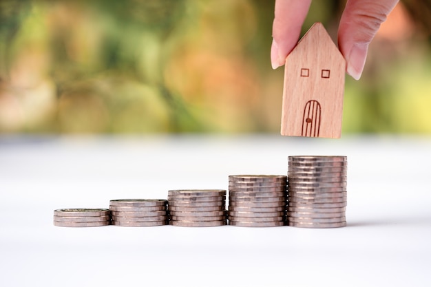 Woman's hand putting house model on coins stack. 