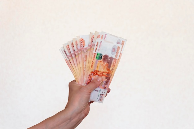 A woman's hand raised up holds Russian money worth five thousand rubles on a light background