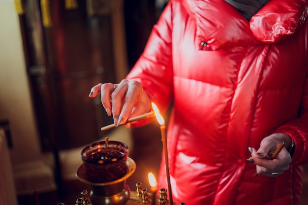 Woman's hand in a red jacket puts a church candle.