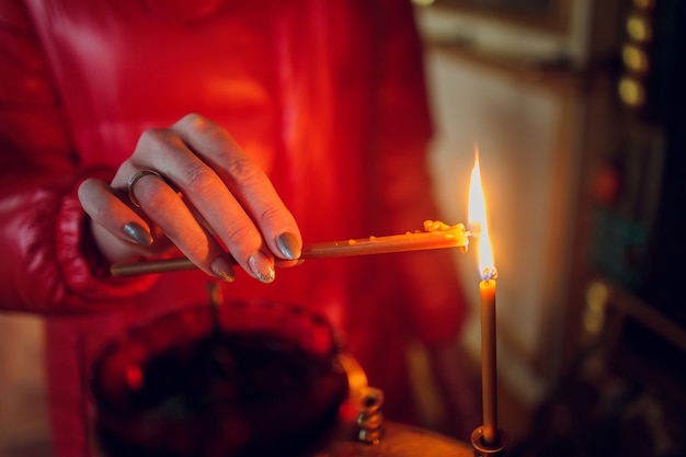 Woman's hand in a red jacket puts a church candle.