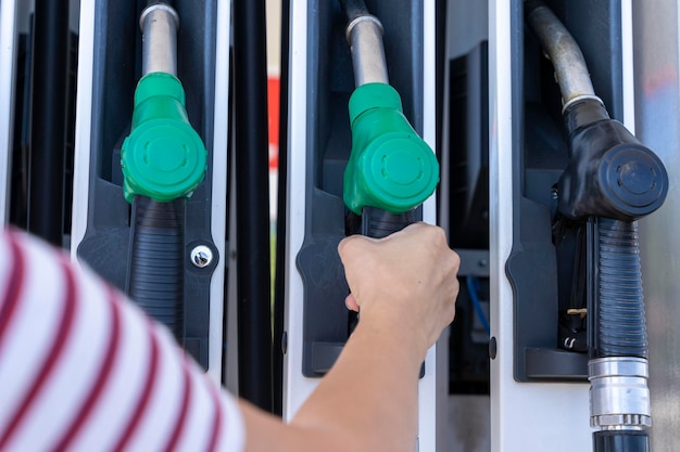 A woman's hand removes a refueling gun from the pump to refuel the car