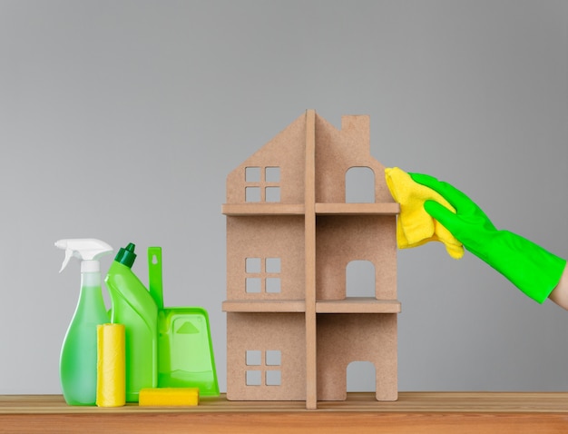 A woman's hand in a rubber glove washes the symbolic house with a green cloth. 