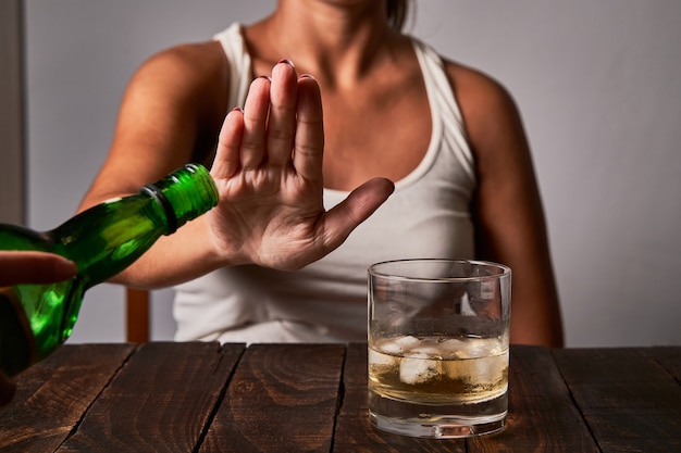 A woman's hand saying don't put any more drink in her glass. Concept of alcoholism and not drinking to drive.