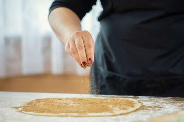 Woman's hand sprinkles cinnamon over the dough