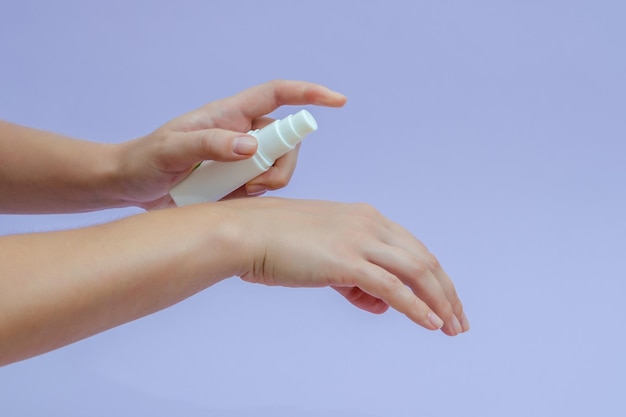 Woman's hand squeezing out cream in white tube isolated on lilac background Beauty concept Tube for cosmetic products