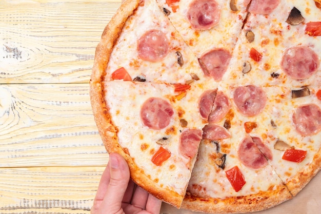 A woman's hand takes a piece of hot capriccioso pizza, top view