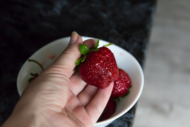 A woman's hand takes a red large strawberry from a white plate