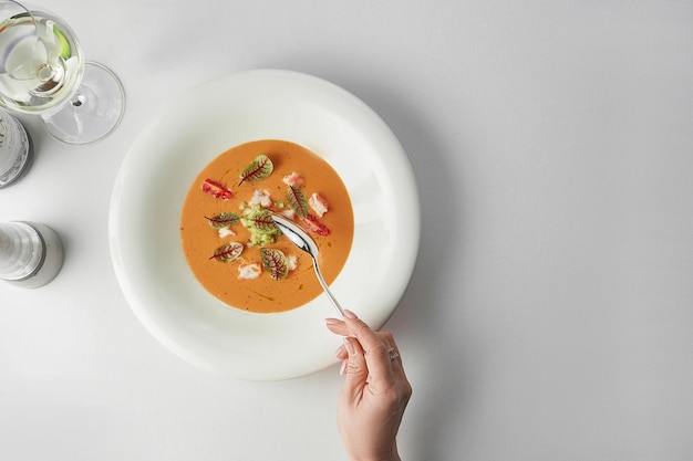 A woman's hand takes a spoonful of pumpkin cream soup with crab White tablecloth Closeup