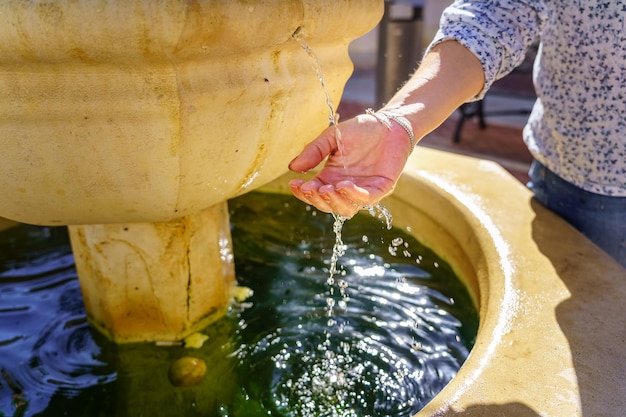 セビリアのエシハ市にあるロマネスク様式の噴水の淡水に触れる女性の手