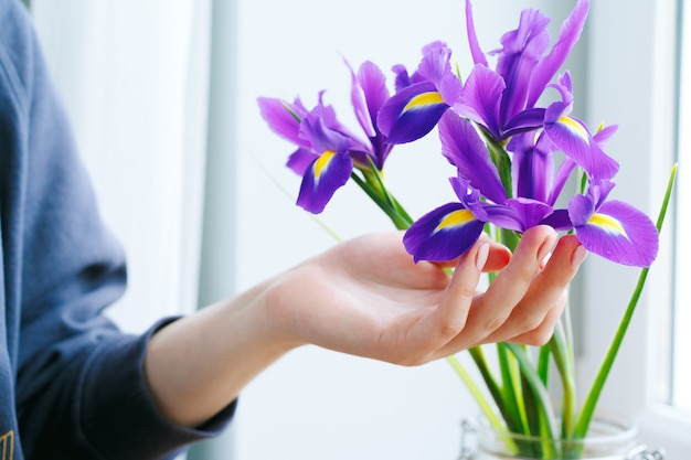 Woman's hand touching irises in a vase on windowsill