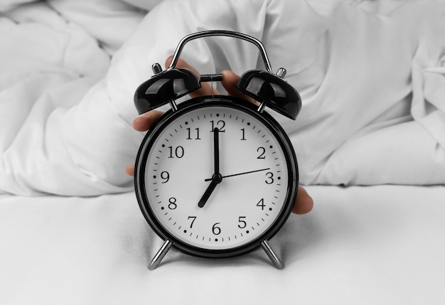 Woman's hand turning off black alarm clock on bed