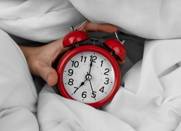 Woman's hand turning off red alarm clock on bed