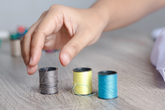 The woman's hand was about to pick up the thread that was placed on the table to sew