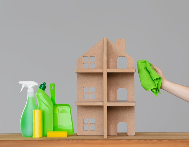 A woman's hand washes the symbolic house with a green cloth, next to the house - a colourful set of tools for cleaning.