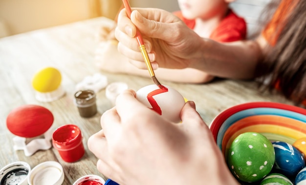 Woman's hand with a brush is drawing a colored pattern on an Easter egg Creative preparation for bright Easter holiday