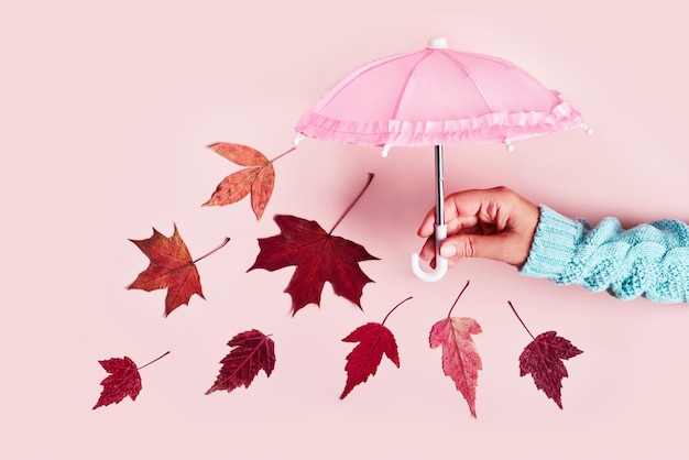 Woman's hand with pink umbrella and falling leaves on pink pastel banner Hello Autumn creative concept