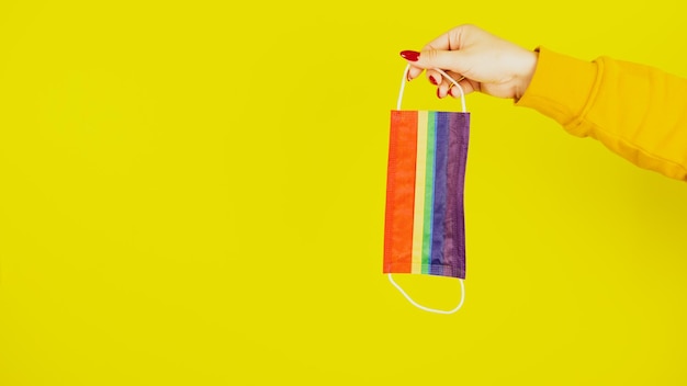 Woman's hand with protective rainbow mask Crop unrecognizable person holding mask lgbt in hand on yellow background