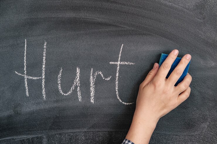 A woman's hand with a sponge erases the chalk-written word hurt from the blackboard